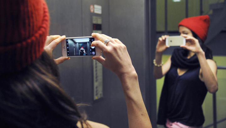 ILLUSTRATION - Eine junge Frau macht in einem Aufzug mit ihrem Smartphone ein Selfie mit ihrem Spiegelbild. Technikbegeistert, immer online, aber auch gesundheits- und umweltbewusst: Das ist nach einer aktuellen Umfrage die Generation Z, also die Gruppe d